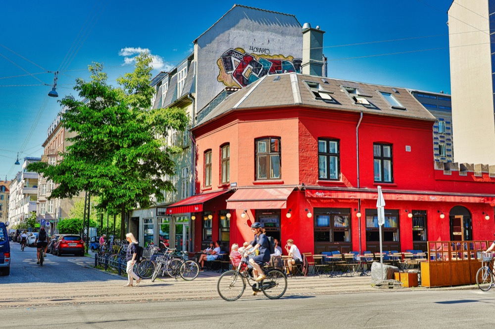 A cyclist passing a red corner café in Nørrebro