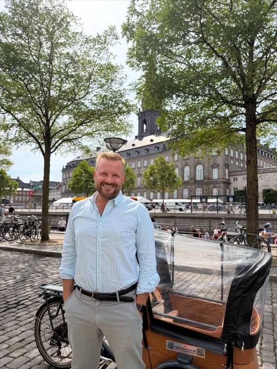 Oliver Wang Hansen standing beside a cargo bike on the cobblestones by a canal in central Copenhagen