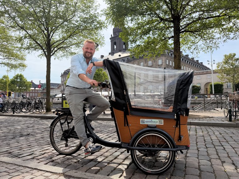 Oliver Wang Hansen sitting on his cargo bike on the cobblestones by a Copenhagen canal