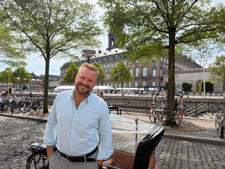 Oliver Wang Hansen standing with his cargo bike, the canal and a palace facade behind him